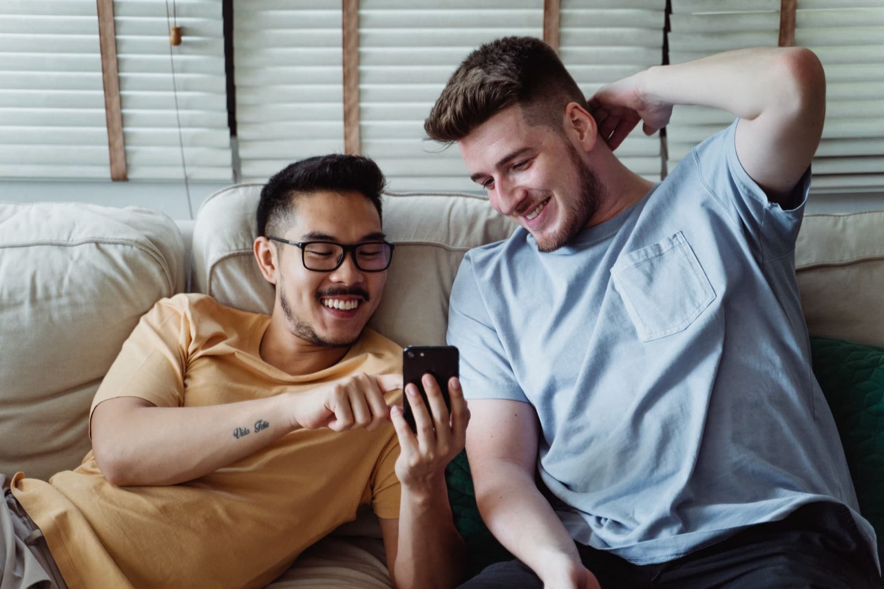 Two partners laughing at one phone on the couch