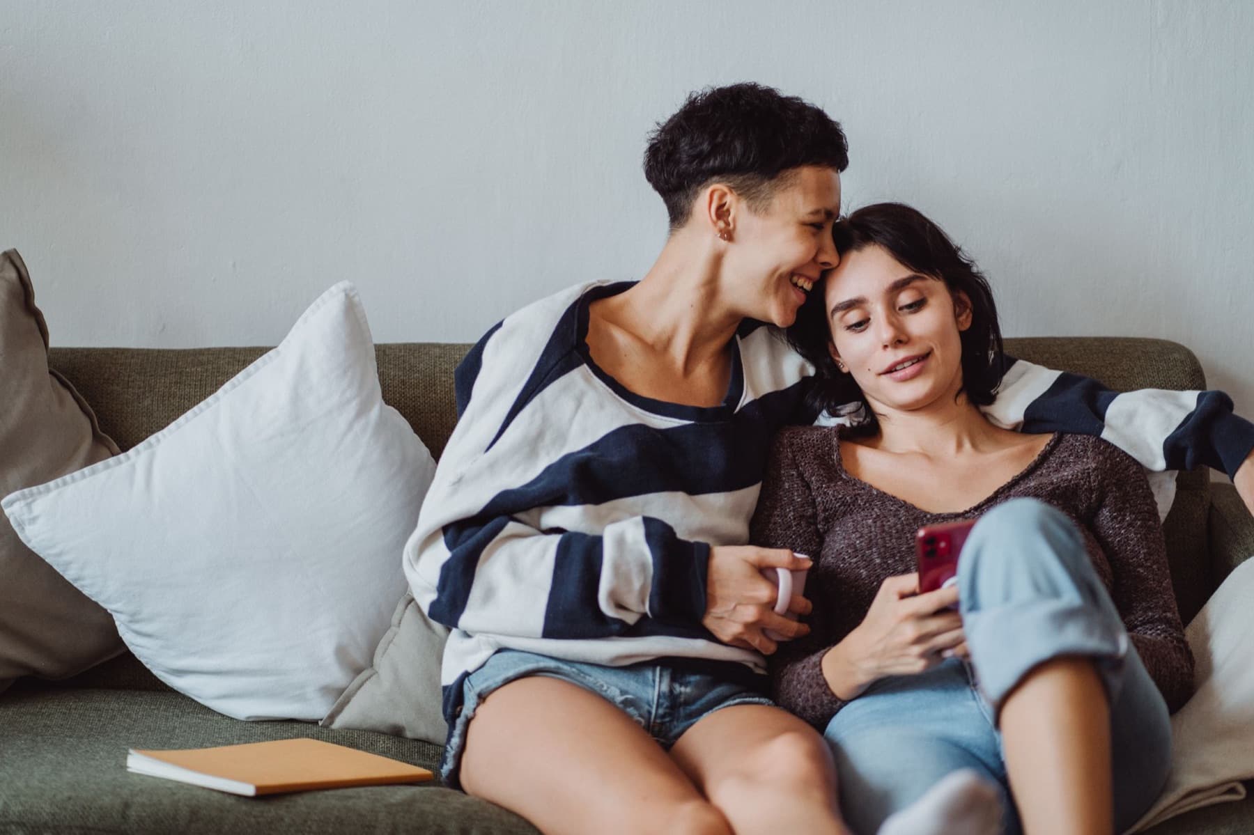 Two partners cuddled on the couch sharing one phone