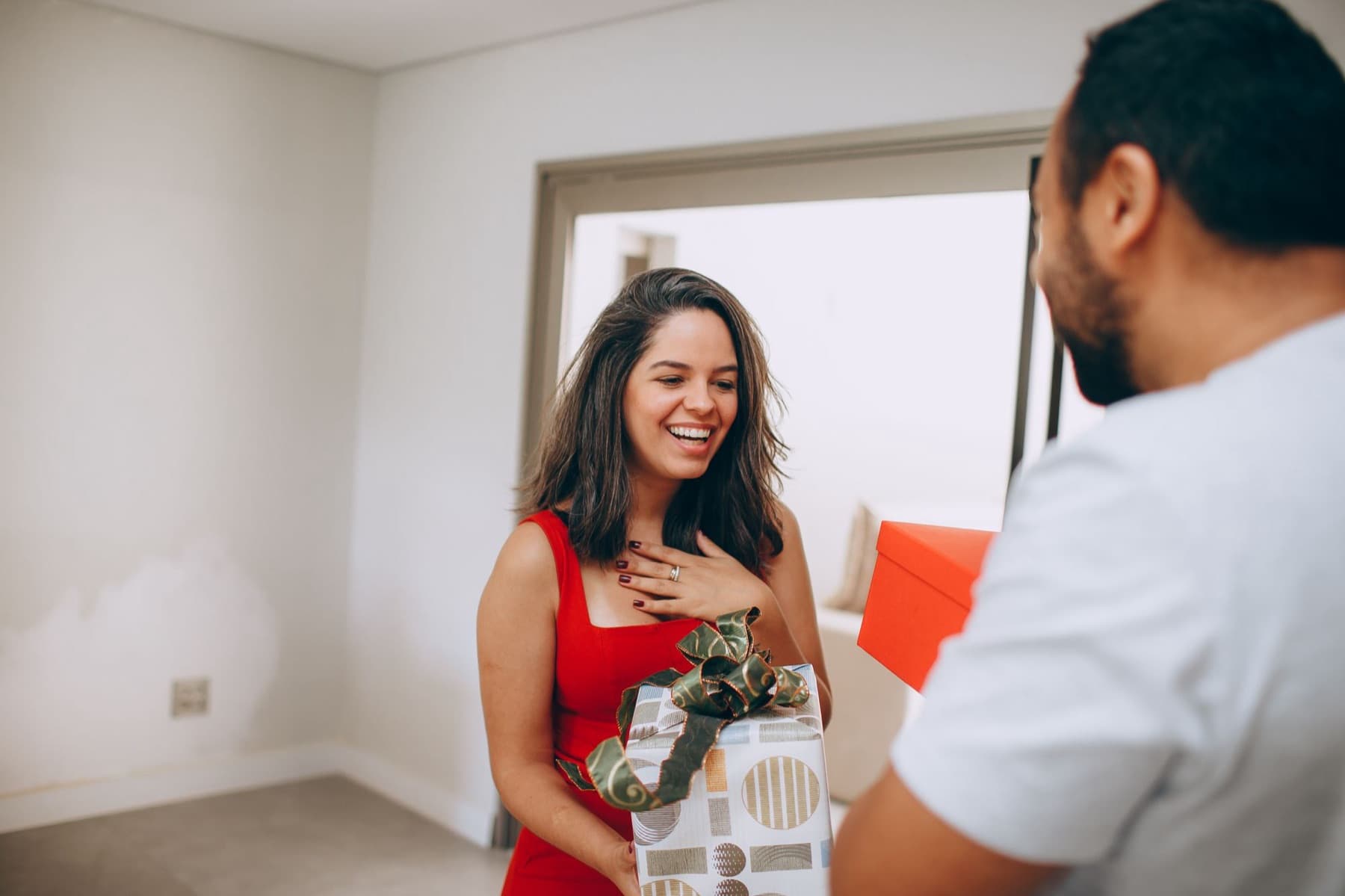 A woman delighted as her partner hands her a wrapped gift