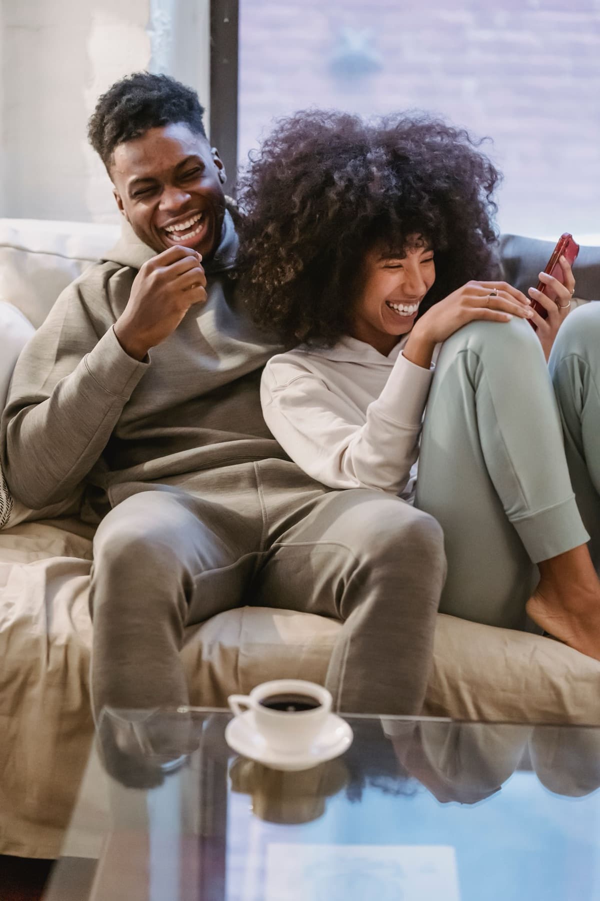 A couple laughing together on the couch, one of them holding a phone