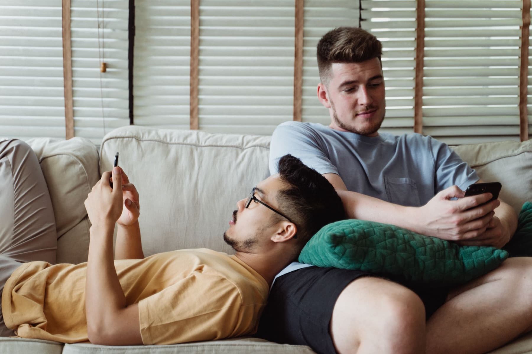 Two partners on the couch, one resting in the other's lap, each on their own phone