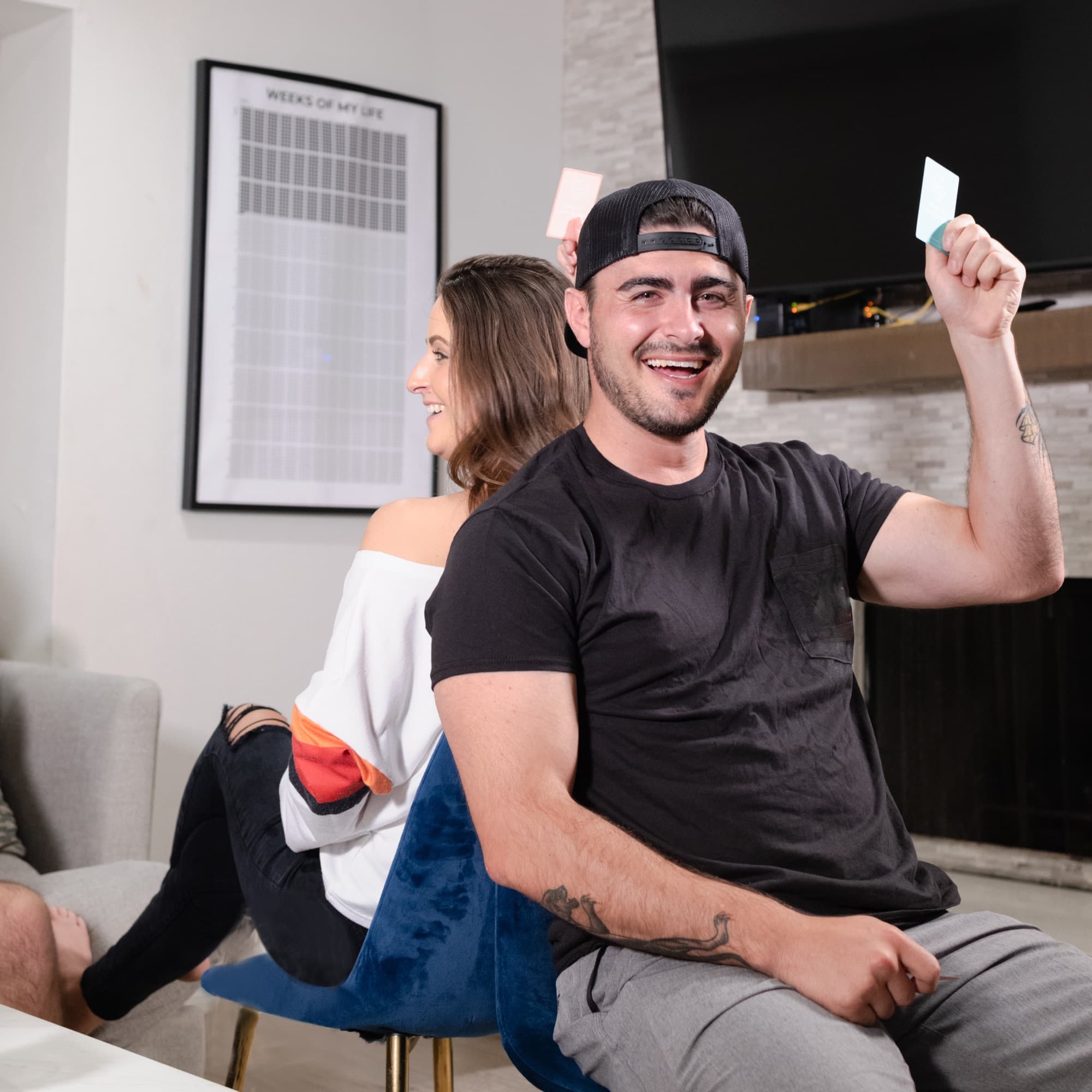 A couple laughing over WhoIs? cards, he in a cap holding teal cards